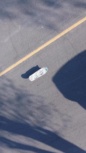 Skateboard on cracked asphalt, casting a long shadow